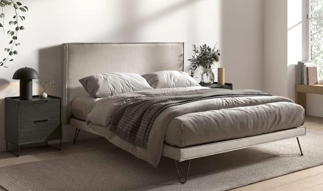 Sommier tapissier tissu beige sur pieds métal dans une chambre claire